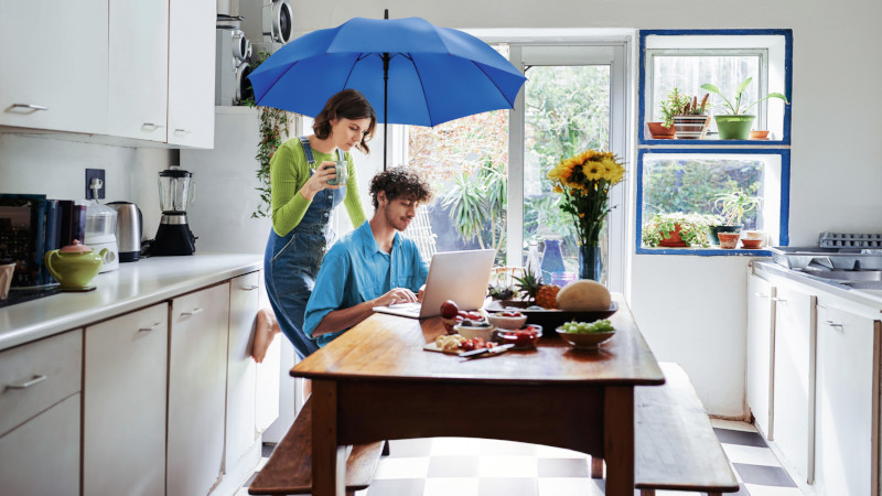 Junges Paar zusammen am Küchentisch mit einem Laptop unter einem blauen Schirm